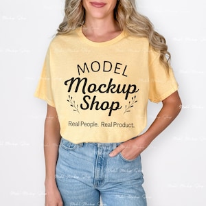 May include: A yellow t-shirt with the text "MODEL Mockup Shop" in black script, with the words "Real People. Real Product." below. The model is wearing light blue jeans.