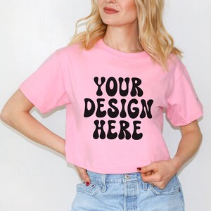 May include: A pink cropped t-shirt with black text that reads "YOUR DESIGN HERE" in a retro font.