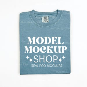 May include: A folded blue t-shirt with the text "MODEL MOCKUP SHOP" and "REAL POD MOCKUPS" in white.