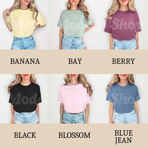 以下が含まれることがあります： 10枚の切り抜き画像のコラージュで、さまざまな色のクロップドTシャツが示されています。Tシャツはすべて同じスタイルで、半袖とクルーネックです。色は、バナナ、ベイ、ベリー、ブラック、ブロッサム、ブルーデニムです。