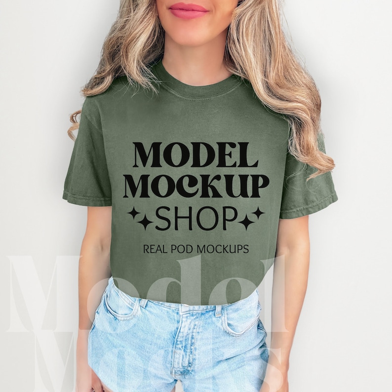 以下が含まれることがあります： 「MODEL MOCKUP SHOP」と「REAL POD MOCKUPS」の文字がプリントされた緑色のTシャツ。モデルは青いデニムのショートパンツを履いています。