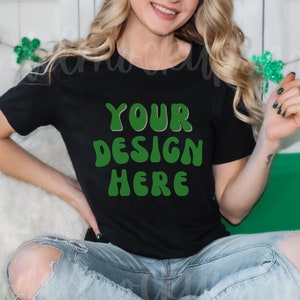 May include: A black t-shirt with the text "YOUR DESIGN HERE" in green letters. The shirt is being worn by a person sitting down.