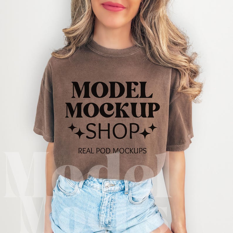 以下が含まれることがあります： 「MODEL MOCKUP SHOP」と「REAL POD MOCKUPS」の文字がプリントされた茶色のクロップドTシャツ。長い茶色の髪の女性が着用しています。