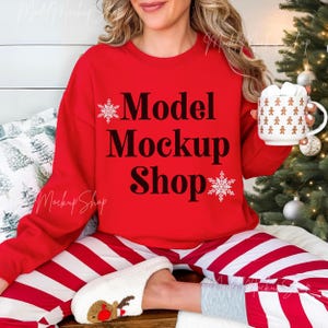 May include: A red sweatshirt with the text "Model Mockup Shop" and snowflake designs. The model is wearing red and white striped pants and white fuzzy slippers.