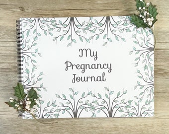 May include: A white pregnancy journal with a spiral binding. The cover features a leafy design in shades of green and gray with the text "My Pregnancy Journal" in black.