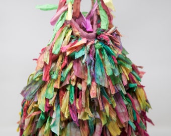 May include: A colourful, fringed tote bag made from recycled fabric scraps. The bag is a vibrant mix of pink, green, yellow, and blue.