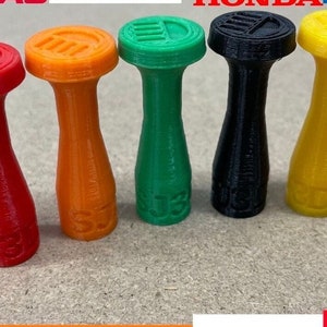 May include: Five different colored plastic push pins with a logo on the top. The colors are red, orange, green, black, and yellow.