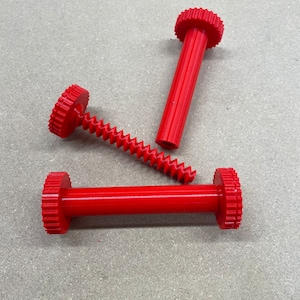 May include: Three red plastic gears with a screw thread. The gears are different sizes and have a ridged surface.