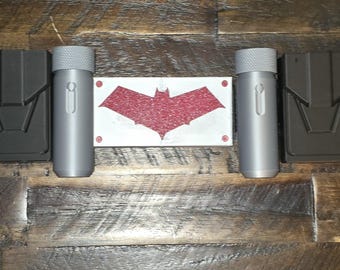 May include: A black utility belt with silver canisters and pouches. A white rectangle with a red bat symbol is centered on the belt. The belt has a black buckle and adjustable strap.