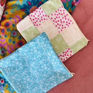 May include: Two fabric zippered pouches. One pouch is light blue with a white floral pattern. The other pouch is made of patchwork fabric with green and pink floral patterns.