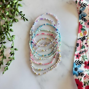 May include: A stack of colorful beaded bracelets with gold accents. The bracelets are made of small, colorful beads and are arranged in a rainbow pattern.