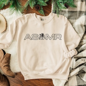 May include: A beige sweatshirt with the text "ASMR" in black lettering. The text includes a microphone icon.
