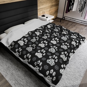May include: Black and white duvet cover with a repeating pattern of paw prints and snowflakes. The duvet cover is on a bed with a white pillow.