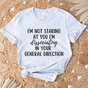 May include: Light blue t-shirt with black text that reads "I'm not staring at you I'm dissociating in your general direction."