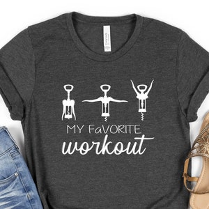 May include: A dark gray t-shirt with a white graphic of three corkscrews in different positions, with the text "MY FAVORITE workout" below.