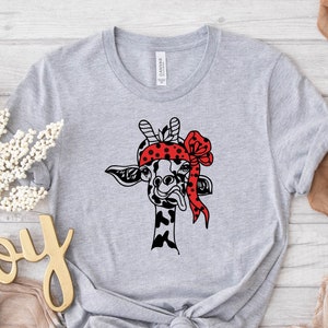 Può includere: Una maglietta grigia con un'illustrazione in bianco e nero di una giraffa che indossa un bandana rosso con pois bianchi. La giraffa sta tirando fuori la lingua.