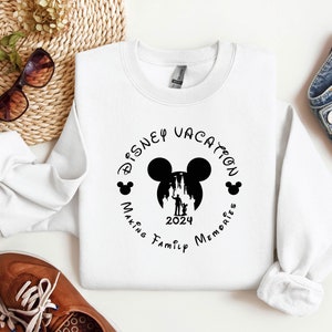 May include: White sweatshirt with a black graphic design that says "Disney Vacation Making Family Memories 2024" with a silhouette of Mickey Mouse's head and the Cinderella Castle.