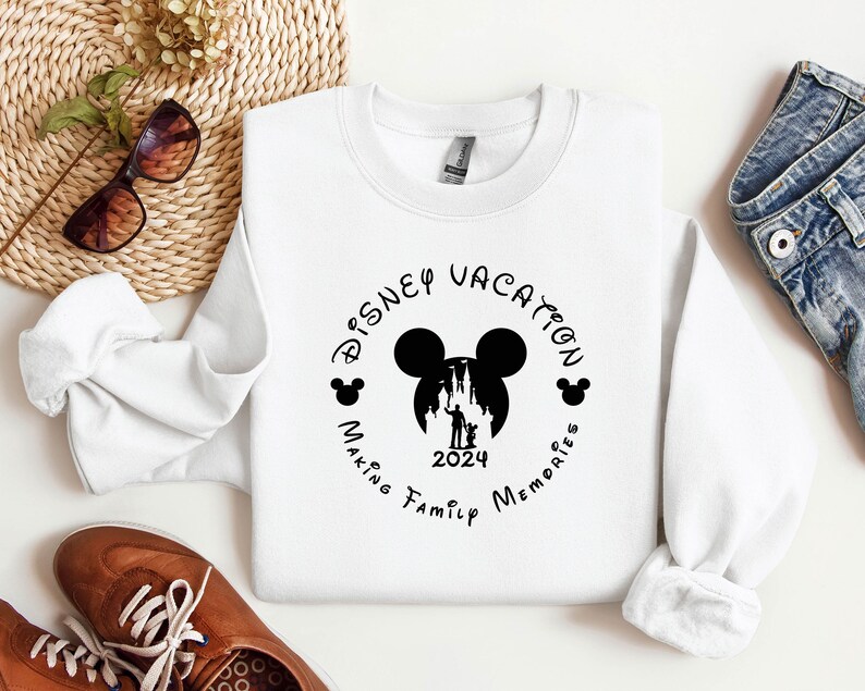 May include: White sweatshirt with a black graphic design that says "Disney Vacation Making Family Memories 2024" with a silhouette of Mickey Mouse's head and the Cinderella Castle.