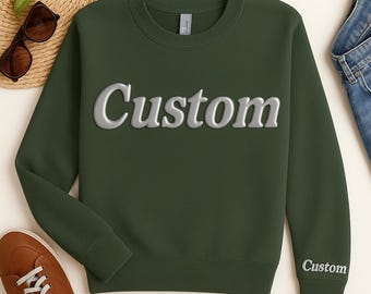 May include: Dark green sweatshirt with the word "Custom" in a 3D silver font across the chest. The word "Custom" is also printed on the left sleeve. The sweatshirt is displayed with sunglasses, a straw hat, brown shoes, and blue jeans.