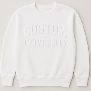 May include: A white crew neck sweatshirt with the words "CUSTOM UNIVERSITY" embossed on the front. The text is in a bold, sans-serif font. The sweatshirt has a classic, casual style.