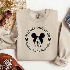 May include: Tan sweatshirt with a black graphic of Mickey Mouse's head with the text "Disney Vacation Making Family Memories 2024" around it.