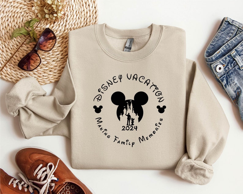 May include: Tan sweatshirt with a black graphic of Mickey Mouse's head with the text "Disney Vacation Making Family Memories 2024" around it.