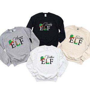 May include: A collection of five crewneck sweatshirts in various colors: gray, black, white, and beige. Each sweatshirt features a graphic of an elf hat and shoes with the words "Mama ELF", "Daddy ELF", "Sister ELF", and "Brother ELF".