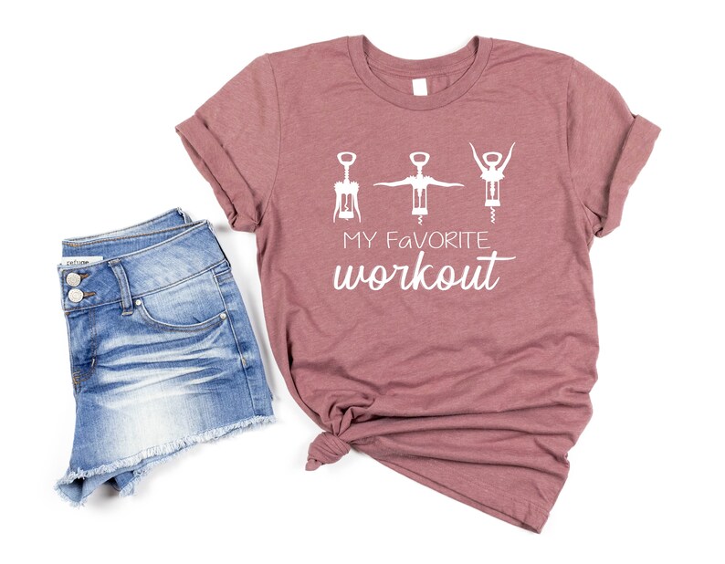 May include: A mauve t-shirt with a white graphic of three wine bottle openers in a workout pose. The text "My Favorite Workout" is printed below the graphic.