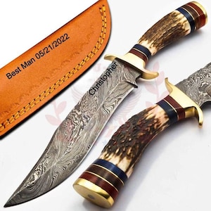 Puede incluir: Cuchillo de caza de acero de Damasco con mango de asta marrón y detalles en latón. La hoja está grabada con el nombre "Christopher". La funda de cuero tiene la inscripción "Best Man 05/21/2022".