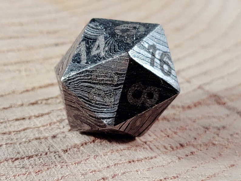 May include: A silver-coloured, 20-sided die with a textured, patterned surface. The die is numbered 1 through 20.