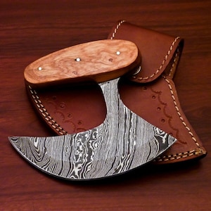May include: A handmade Damascus steel axe with a wooden handle and a leather sheath. The axe has a unique, wavy pattern on the blade.