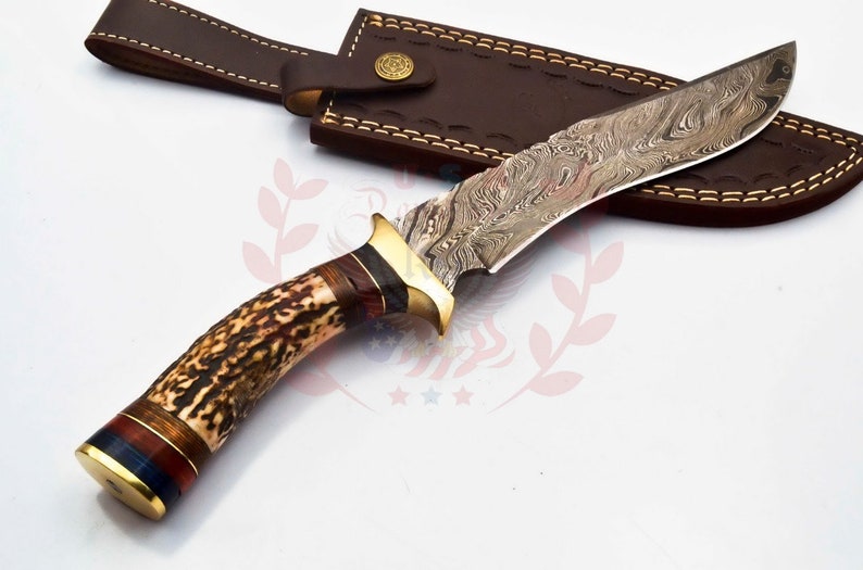 Puede incluir: Un cuchillo de caza con mango de asta de ciervo marr&oacute;n y hoja de acero damasco. El cuchillo viene con una funda de cuero marr&oacute;n.