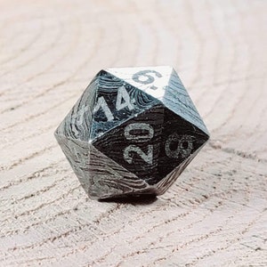 May include: A silver-coloured, 20-sided die with black numbers. The die has a textured, patterned surface.