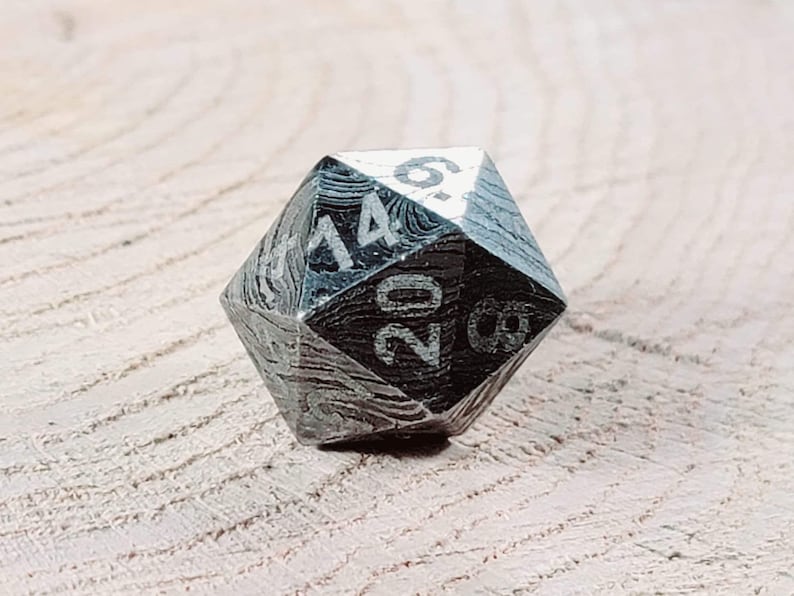 May include: A silver-coloured, 20-sided die with black numbers. The die has a textured, patterned surface.