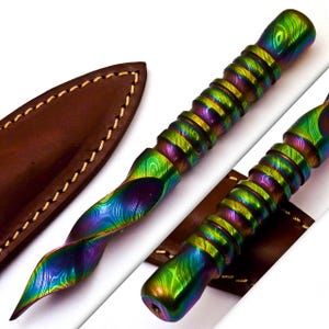 May include: A multi-colored, Damascus steel knife with a twisted handle and a brown leather sheath. The knife features a vibrant pattern of blues, greens, and purples. The sheath is stitched with a contrasting thread.