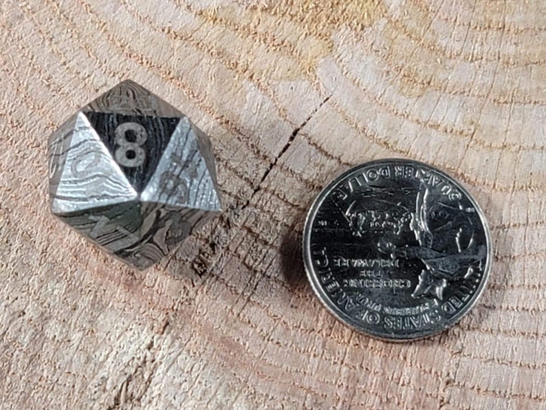 May include: A silver, eight-sided die with a patterned surface, showing the number eight, next to a US quarter.