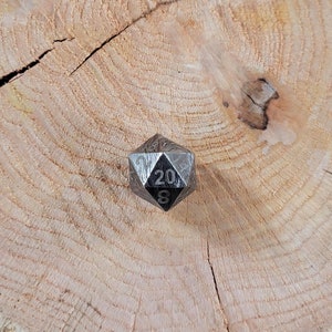 May include: A black metal twenty-sided die with a patterned surface and the numbers 20 and 8 visible.