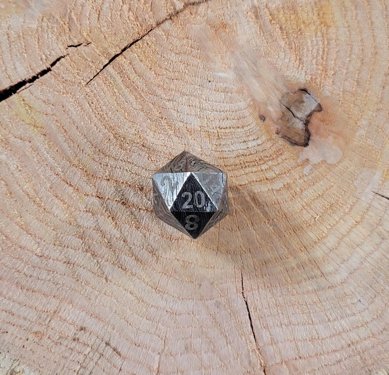 May include: A black metal twenty-sided die with a patterned surface and the numbers 20 and 8 visible.