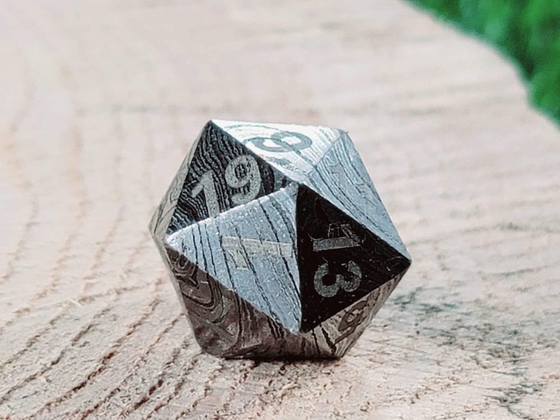 May include: A silver and black metal d20 dice with a unique patterned design. The numbers 1, 3, 9, and 19 are visible on the dice.