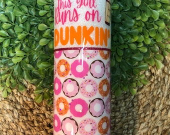 May include: White glitter tumbler with the text "This girl runs on Dunkin'" in pink and orange. The bottom half of the tumbler is covered in a pink and orange donut pattern.