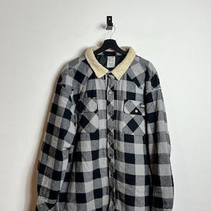 Peut inclure: Une chemise en flanelle à carreaux noirs et gris avec un col doublé de sherpa. La chemise a une fermeture boutonnée à l'avant et deux poches poitrine.