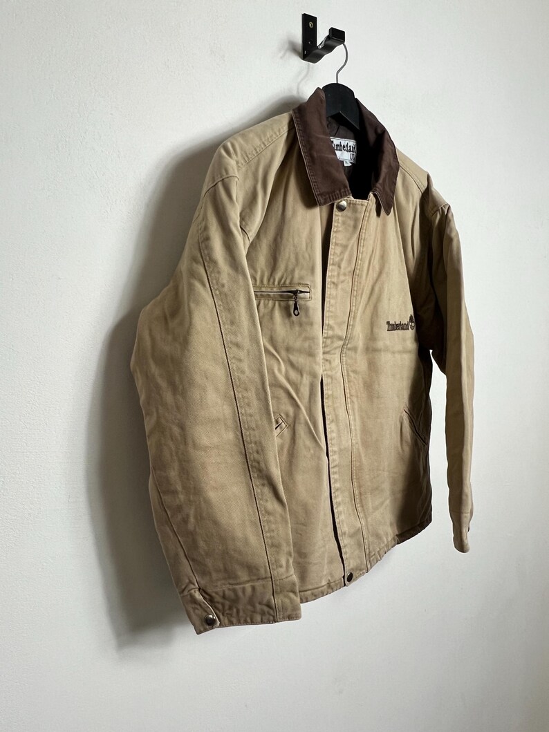 May include: A tan work jacket with a brown corduroy collar and a brown embroidered logo that says "Timberland" on the left chest.
