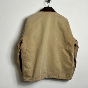 May include: A tan work jacket with a brown corduroy collar. The jacket has a zipper closure and two front pockets.