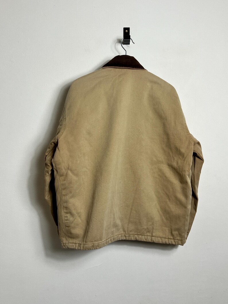 May include: A tan work jacket with a brown corduroy collar. The jacket has a zipper closure and two front pockets.