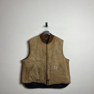 Może przedstawiać: Brązowa pikowana kamizelka Carhartt z zamkiem błyskawicznym i naszywką z logo Carhartt z przodu. Kamizelka ma zużyty wygląd i wisi na wieszaku.