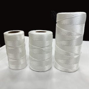 May include: Three spools of white cord, varying in size, are arranged in a row. The cord is tightly wound, creating a textured surface. The spools have a cylindrical shape with a brown core visible at the top.