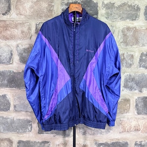 May include: A long-sleeve windbreaker jacket featuring a color-blocked design in shades of dark navy blue and bright purple. The jacket has a full-length front zipper, a high collar, elasticized cuffs and hem, and the word "Mistral" embroidered.