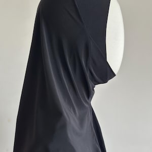 May include: A black hijab, a traditional head covering, is draped over a white mannequin head. The fabric is smooth and appears to be lightweight, with soft folds and a subtle sheen. The head covering is designed to cover the hair and neck.