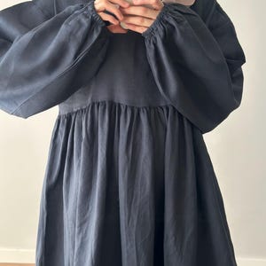 May include: A dark charcoal gray dress featuring long, voluminous sleeves with elasticized cuffs and a gathered, flowing skirt. The garment has a round neckline and a relaxed, loose-fitting silhouette that extends downward from the bodice.
