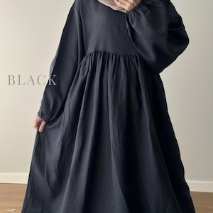May include: A long-sleeved black dress with a gathered waistline and a full, flowing skirt. The garment features a round neckline and elasticized cuffs on the sleeves. The word BLACK is printed in a light gray serif font on the left side.